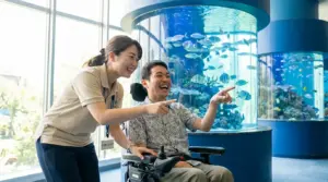 水族館の水槽前でガイドヘルパーと利用者様が一緒に魚を見て笑顔で楽しむ移動支援の様子
